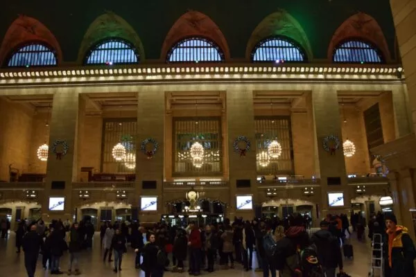 Viele Menschen stehen in der Grand Central Station, die winterlich dekoriert mit Kränzen und grünen und roten Lichtern ist