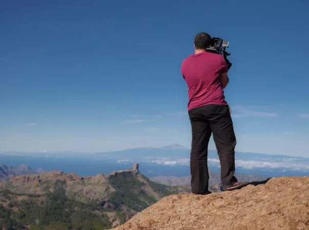 Mann mit Kamera auf Schulter auf einem Felsen