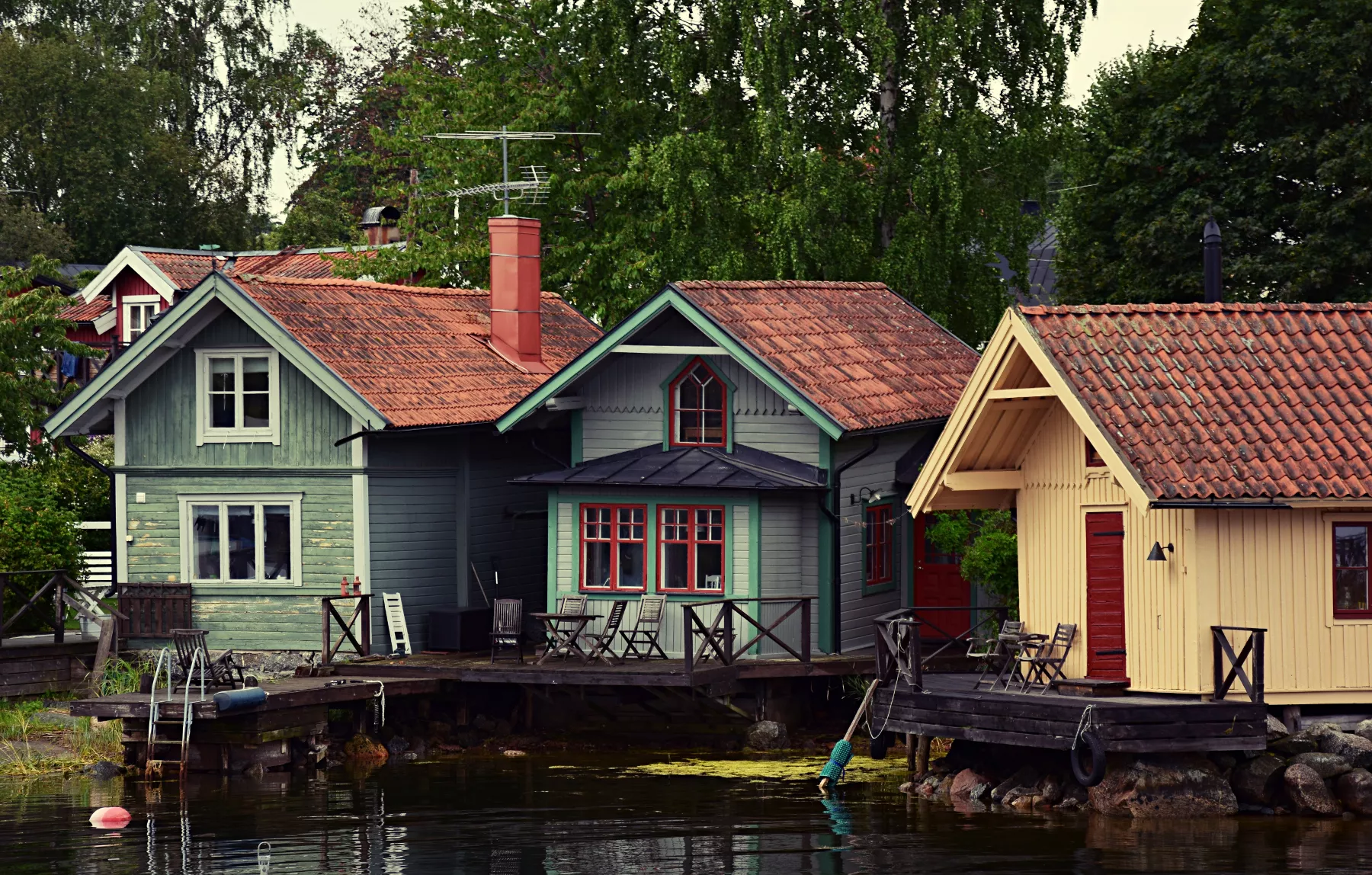Direkt am Wasser stehen 3 Holzhütten im typisch schwedischem Stil und unterschiedlichen Farben.