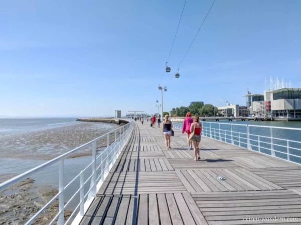 Fußgänger auf Uferpromenade mit Seilbahn in Lissabon