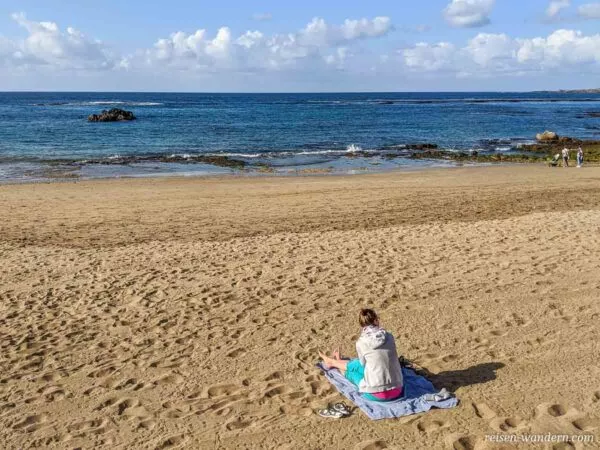 Frau sitzend auf einem Badehandtuch am Srand Playa Las Canteras