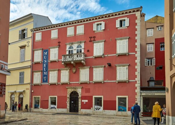 Ein rotes Gebäude mit vielen kleinen Fenstern und einem Banner auf dem "Museum" zu lesen ist 