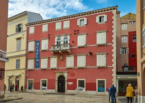 Ein rotes Gebäude mit vielen kleinen Fenstern und einem Banner auf dem "Museum" zu lesen ist 