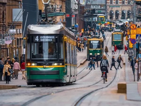 Auf einer Straße in Helsinki fahren mehrere Straßenbahnen, daneben laufen viele Fußgänger 