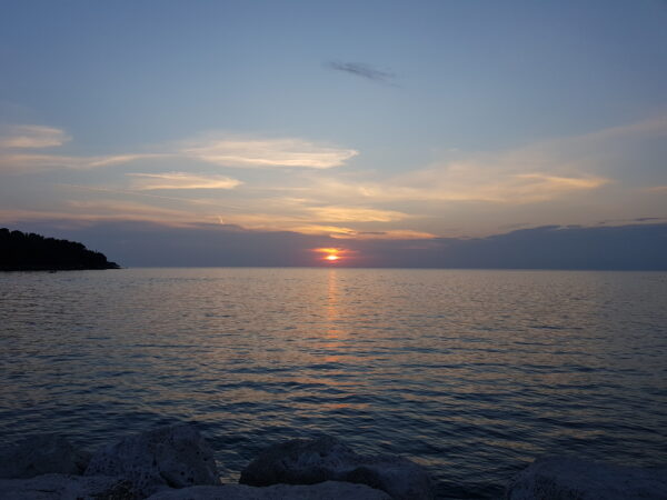 Der Blick auf einen Sonnenuntergang über dem Meer, am linken Rand ist noch etwas Küste erkennbar 