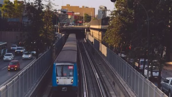 Eine blaue Metro fährt in der Mitte des Bildes auf Schienen entlang. Zu beiden Seiten ist eine Straße mit Autos zu erkennen, im Hintergrund Gebäude der Hauptstadt Chiles