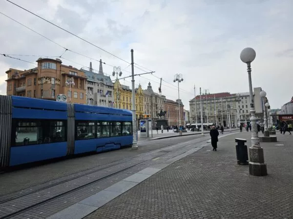 Eine blaue Tram fährt über einen großen Platz, der von Häusern eingerahmt ist