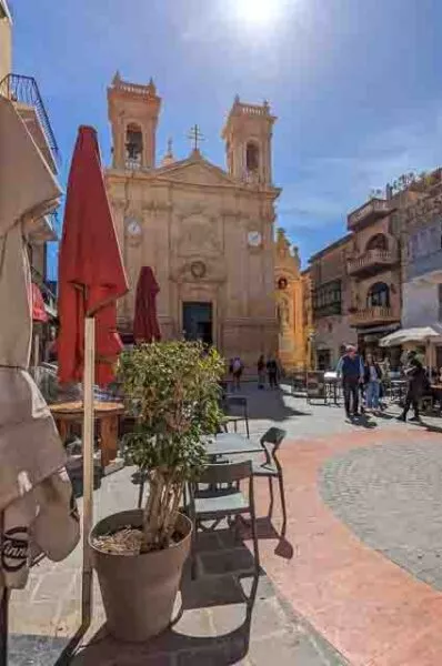 Ein gepflasterter Platz vor einer Kirche, auf dem Stühle und Tische diverser Restaurants stehen 