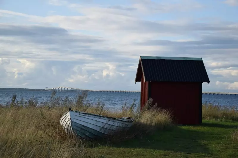 Neben einer roten Holzhütte steht ein Paddelboot, im Hintergrund der Kalmarsund