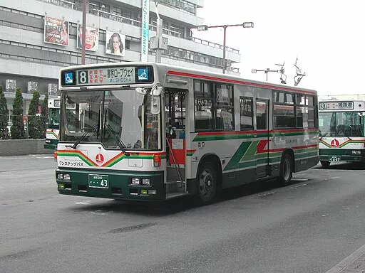 Ein weiß-grüner Bus der Stadt Himeji fährt auf einer Straße. Ihm folgt ein zweiter im Hintergrund.