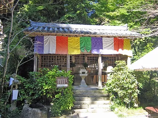 Ein kleines Tempelgebäude mitten im Grünen, das mit bunten Stofftüchern behangen ist 