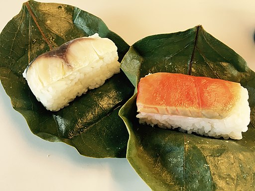 Auf zwei grünen Kaki-Blättern liegen zwei verschiedene Arten Sushi