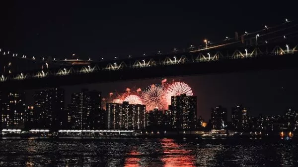 Das sich nachts im Wasser spiegelnde Feuerwerk über New York hinter der Skyline Manhattans und der Brooklyn Bridge