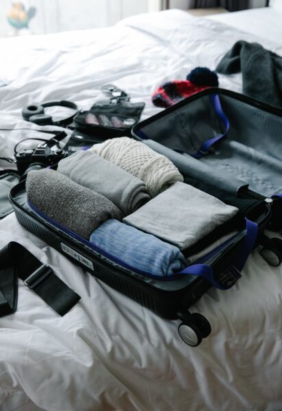 Ein geöffneter, zur Hälfte gefüllter Koffer liegt auf einem Bett, drumherum verschiedene Sachen und Wertgegenstände