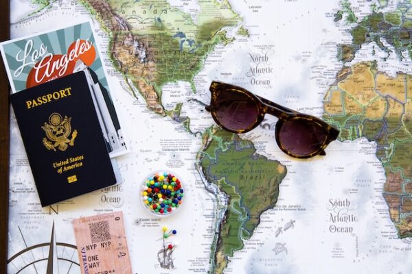 Auf einer Weltkarte liegt eine Sonnenbrille, ein Reisepass, eine Postkarte und ein Fahrtticket