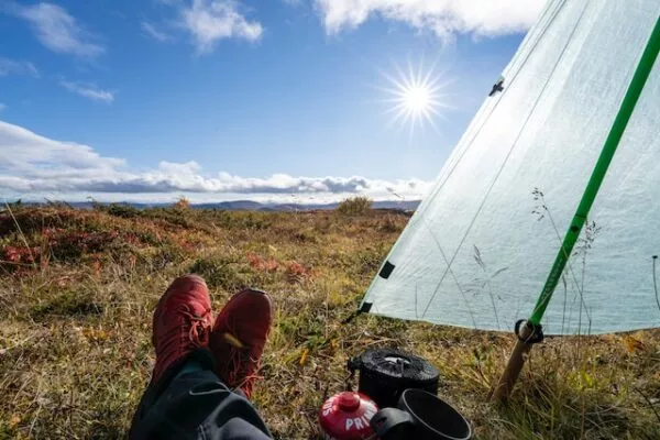 Füße einer liegenden Person, daneben ein Zelt mit Blick auf die Landschaft