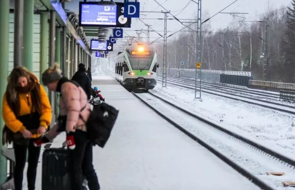 Ein einfahrender Zug an ein verschneites Gleis, auf dem Menschen warten.